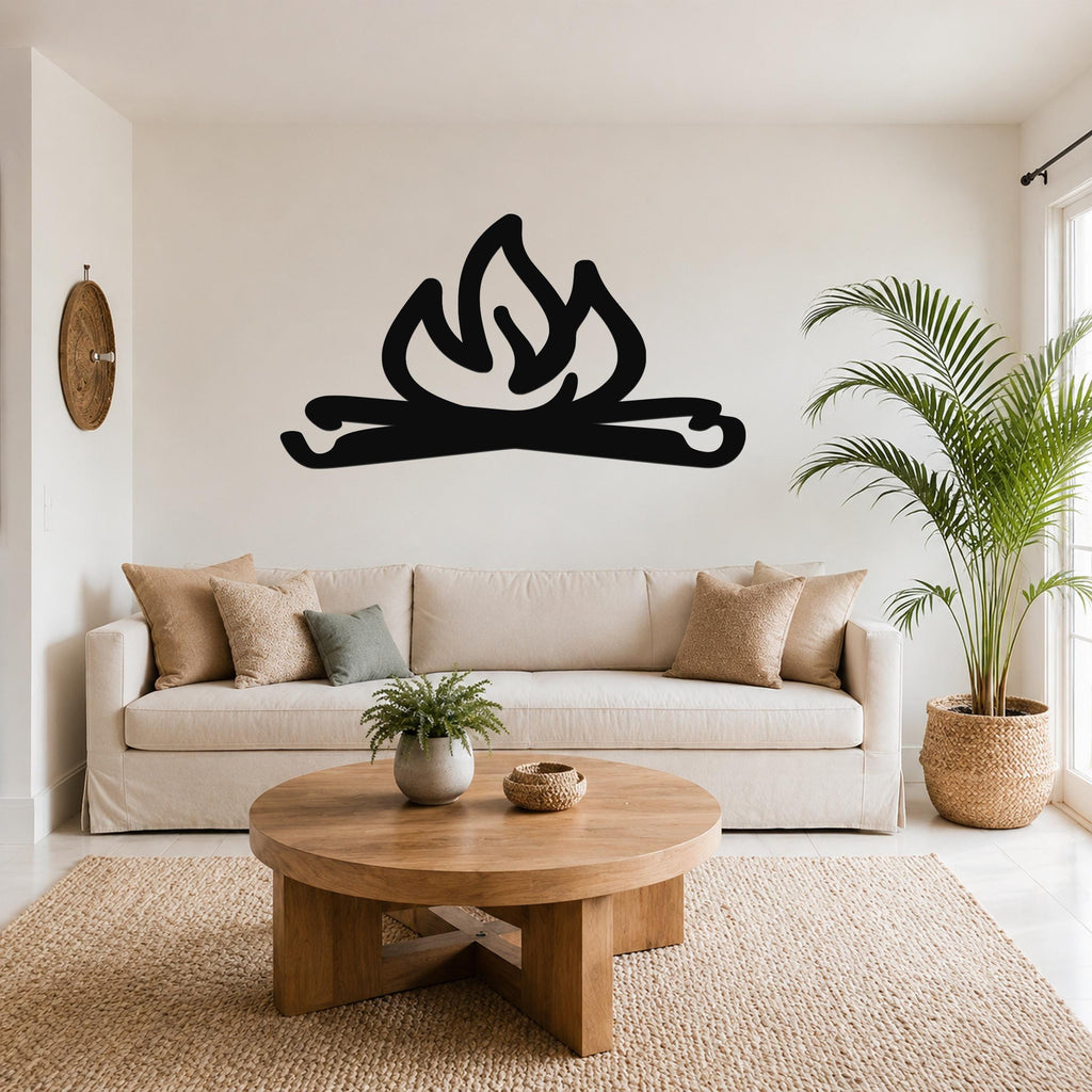 Black metal campfire wall art with flame and log cutouts, mounted above a beige sofa in a living room.