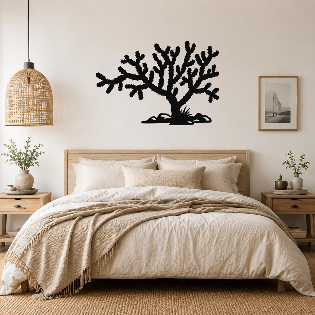 Black metal Cholla cactus wall art silhouette with branching arms and spines, mounted above a bed in a neutral bedroom.