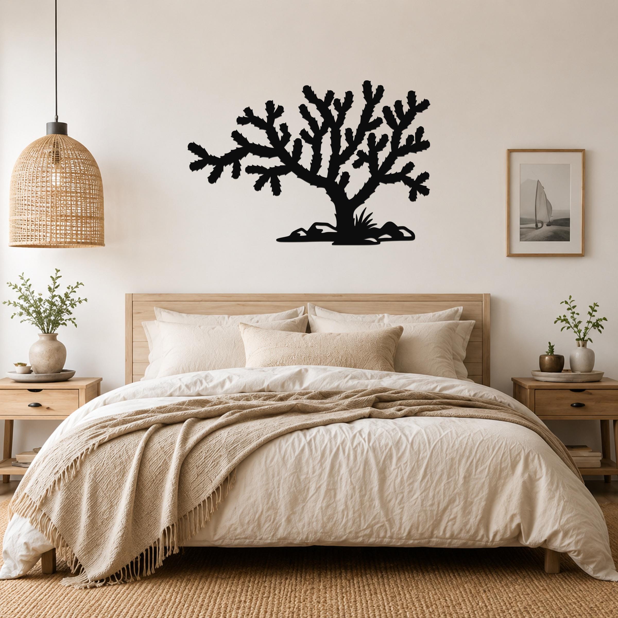 Black metal Cholla cactus wall art silhouette with branching arms and spines, mounted above a bed in a neutral bedroom.
