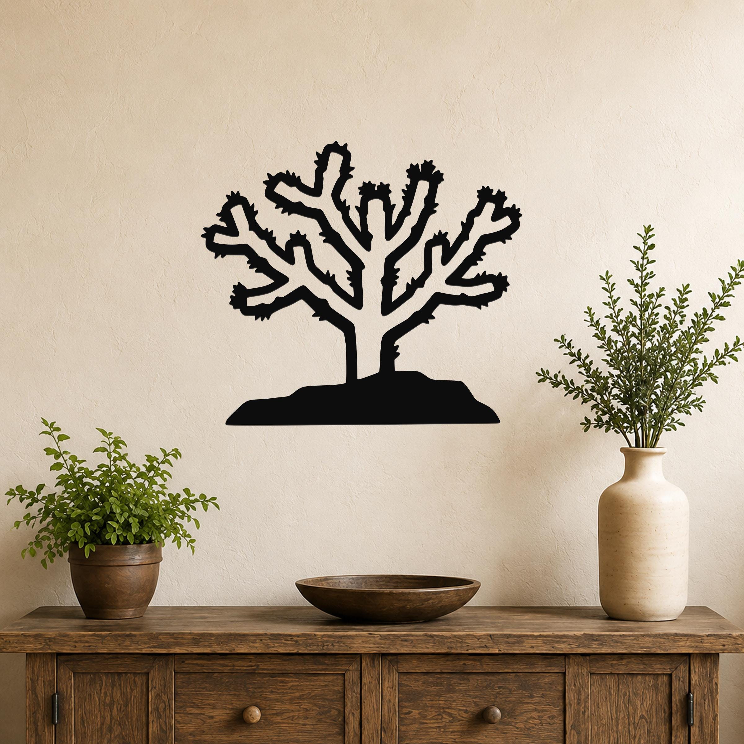 Black metal Cholla cactus wall art with branching silhouette, mounted on a beige wall above a wooden console table.