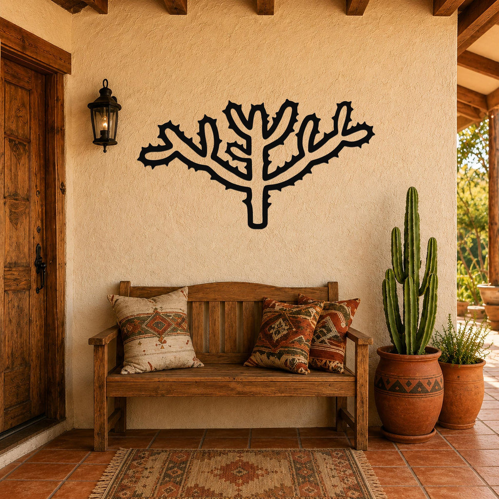 Black metal wall art in the silhouette of a cholla cactus with branching arms and spines, mounted on a stucco wall above a wooden bench in a patio entryway.