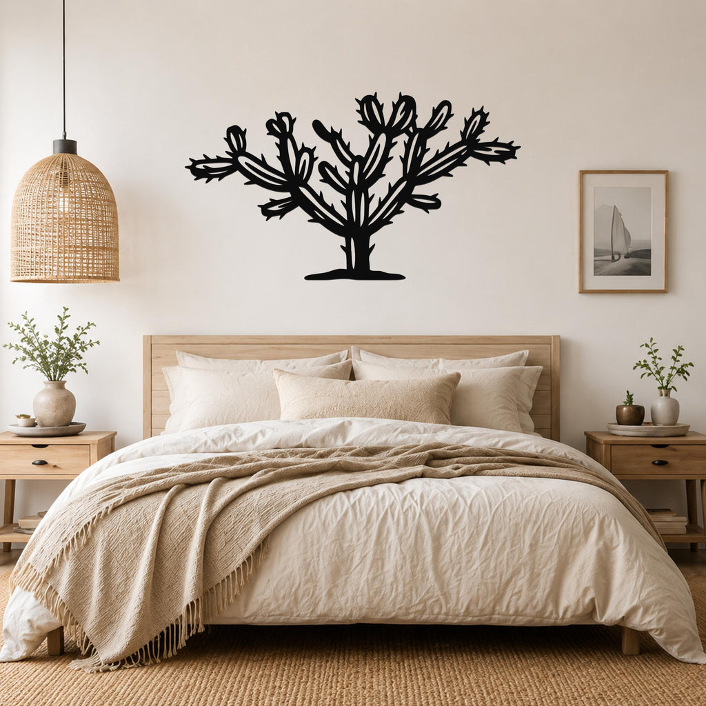 Black metal Cholla cactus wall art silhouette with branching arms and spines, mounted above a bed in a neutral bedroom.