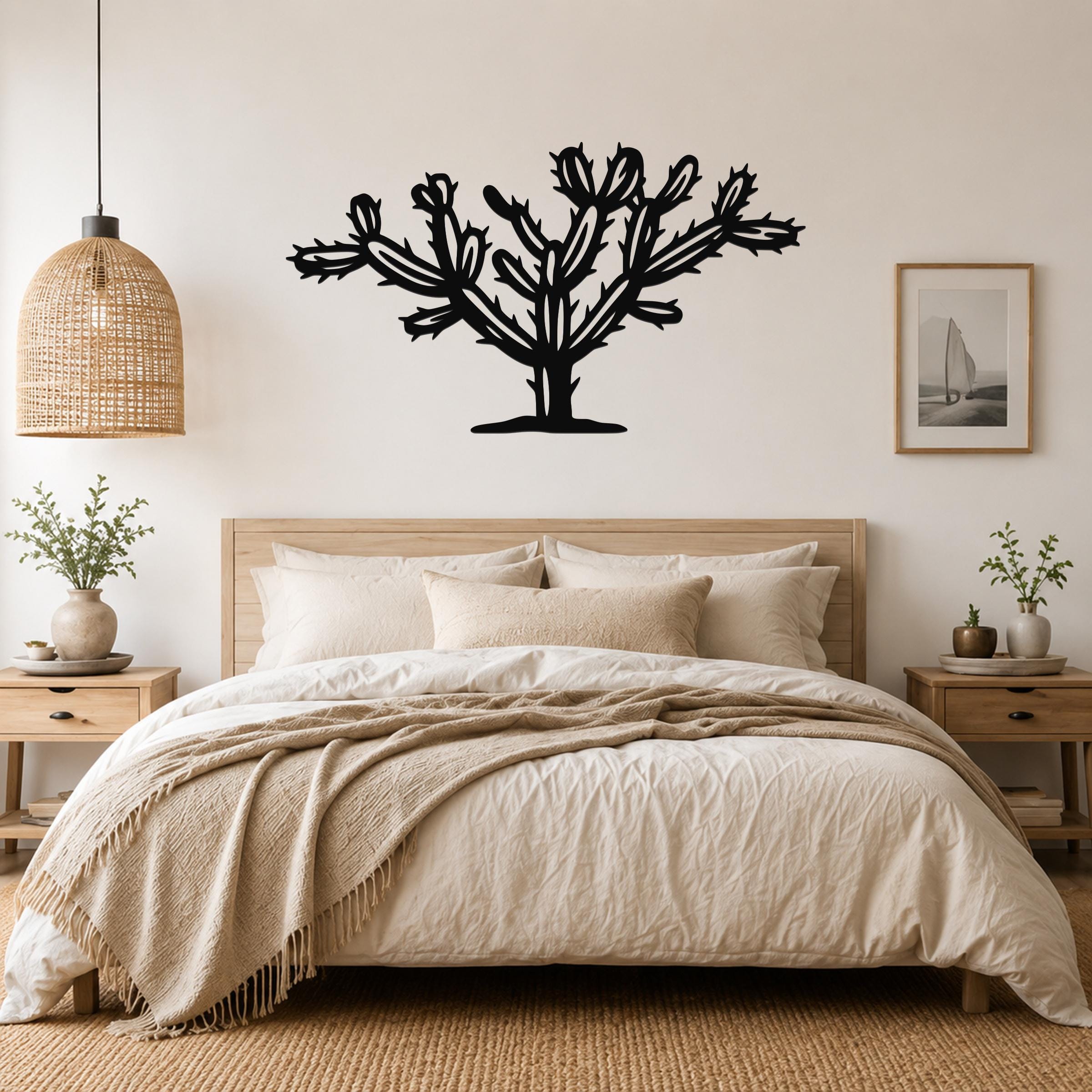Black metal Cholla cactus wall art silhouette with branching arms and spines, mounted above a bed in a neutral bedroom.