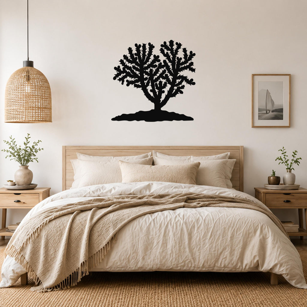 Black metal Cholla cactus wall art with branching silhouette, mounted above a bed in a neutral bedroom.