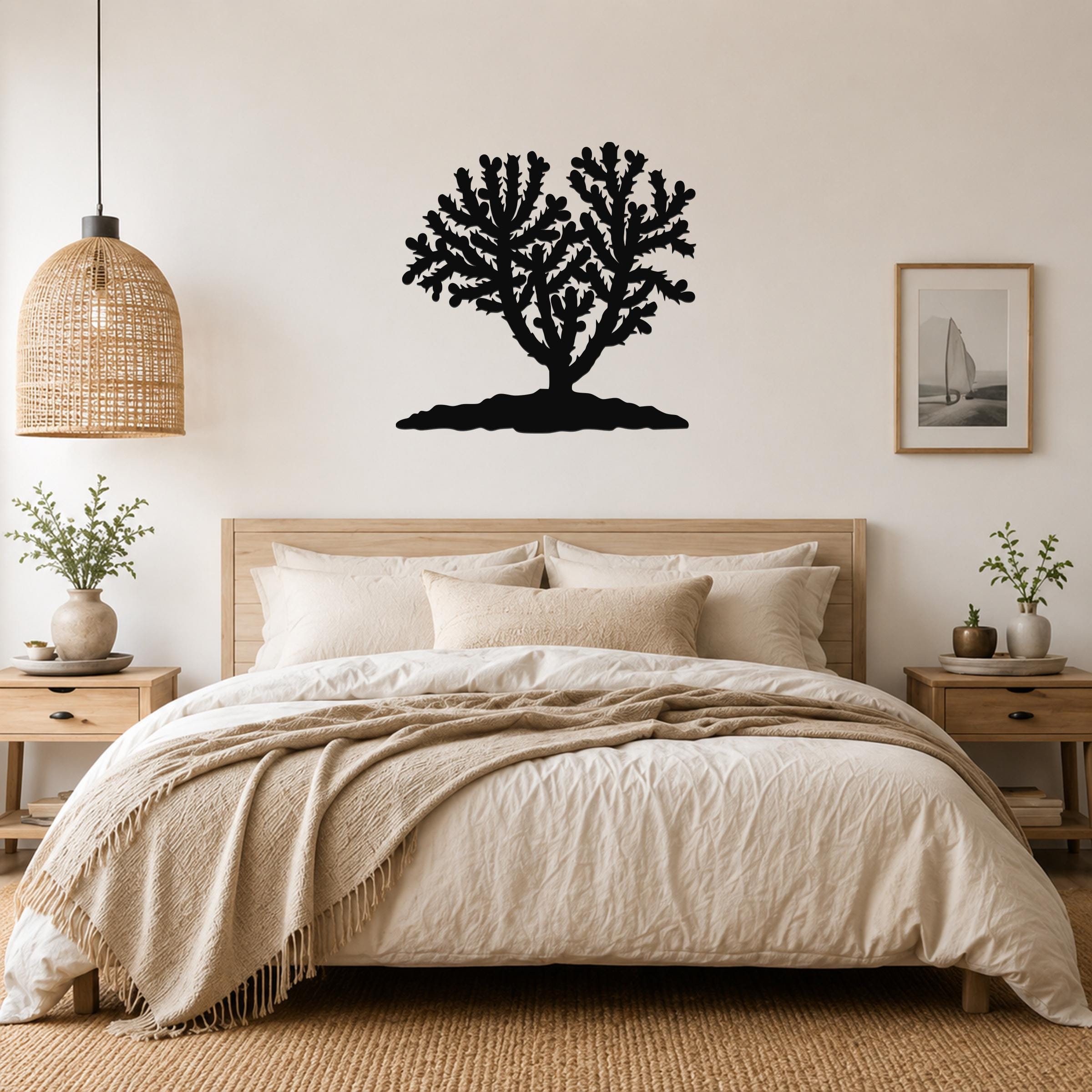 Black metal Cholla cactus wall art with branching silhouette, mounted above a bed in a neutral bedroom.