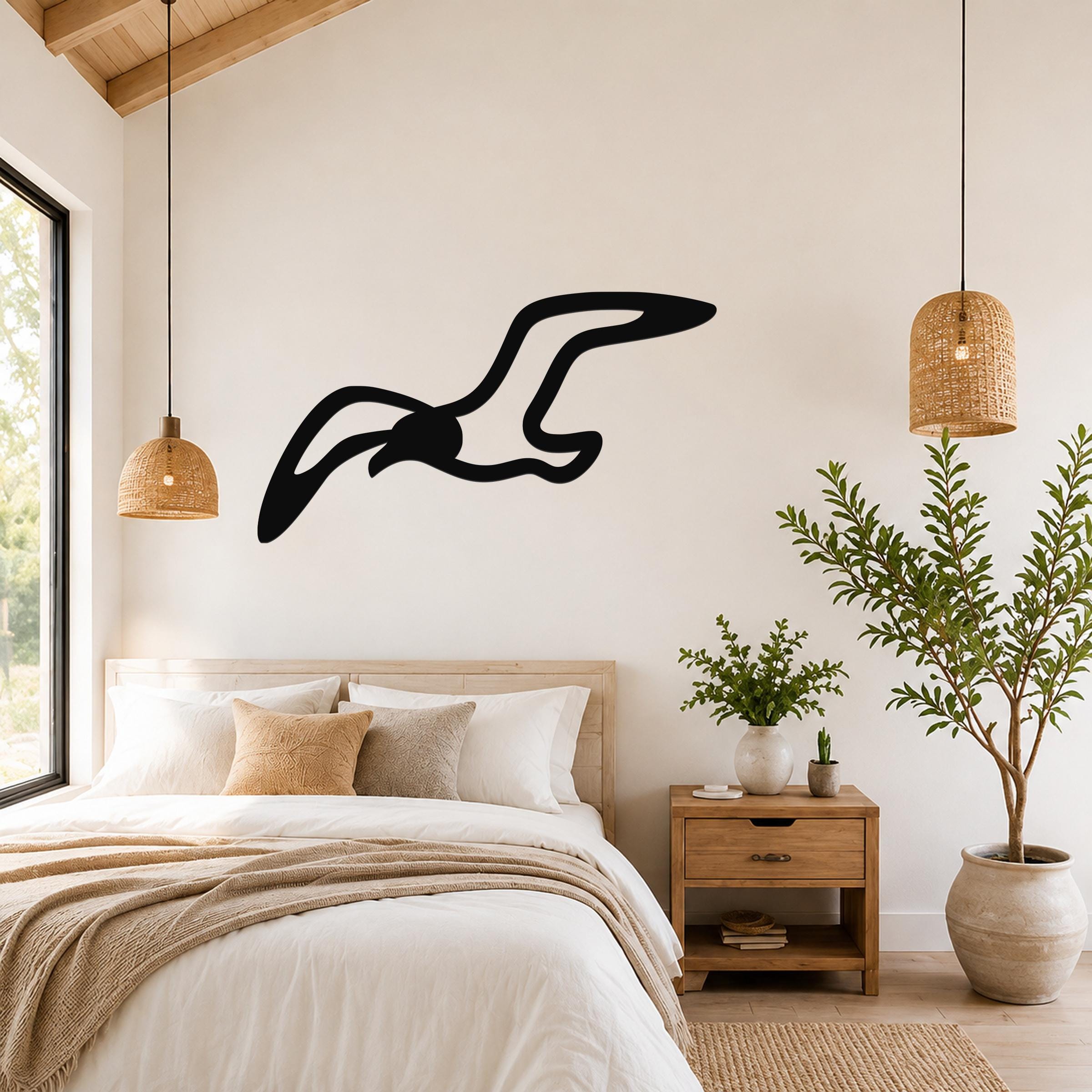 Black metal seagull wall art with flowing wing cutouts, mounted above a bed in a bright bedroom.
