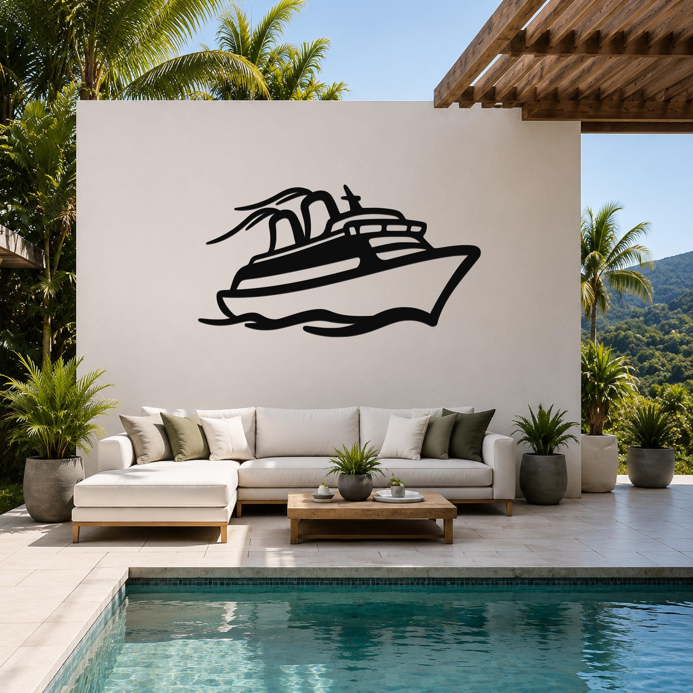 Black metal wall art featuring a cruise ship silhouette with motion lines, mounted on a white outdoor wall above a sofa in a patio living area.