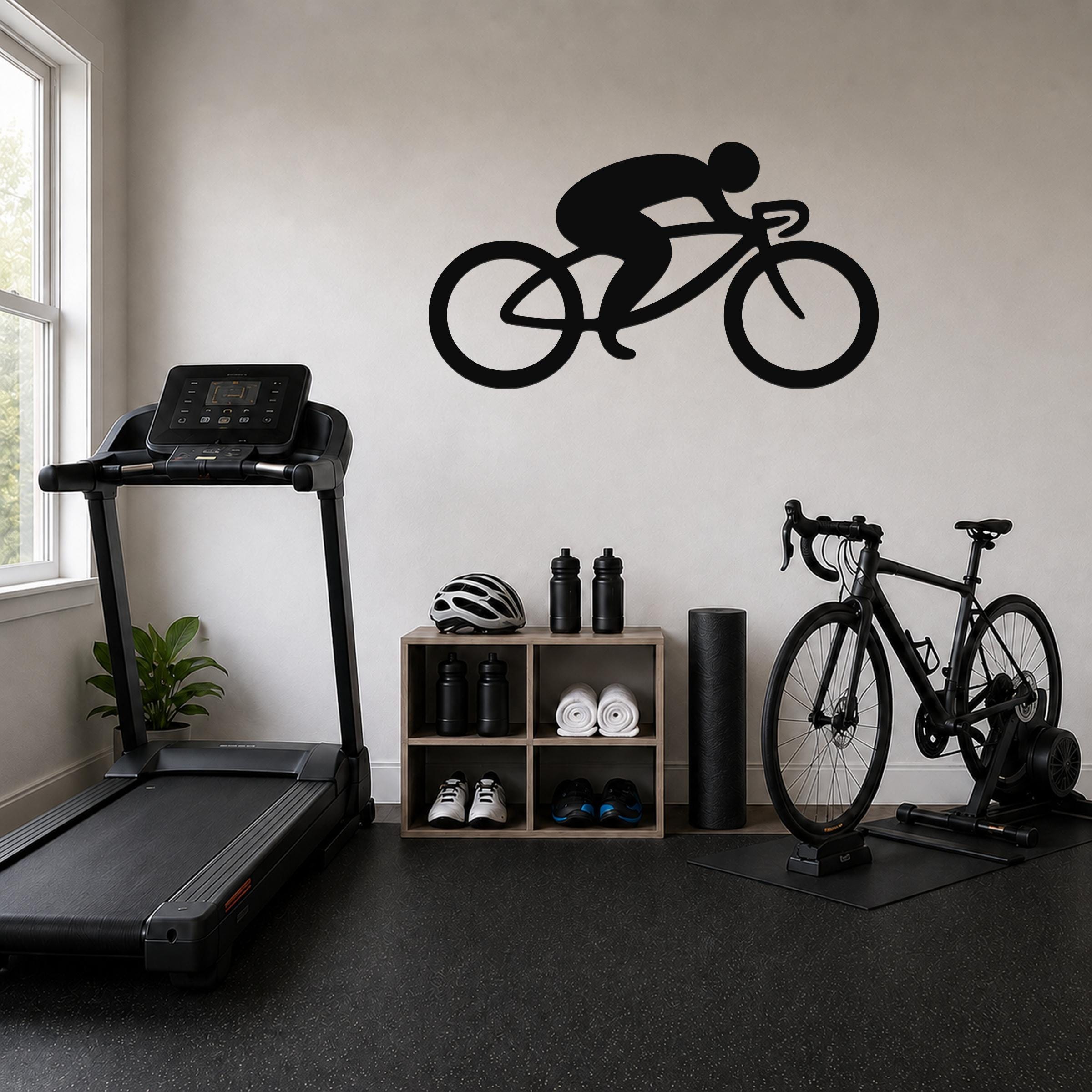 Black metal cycling wall art silhouette of a rider on a road bike, mounted on a light-colored wall above a wooden storage unit in a home gym.