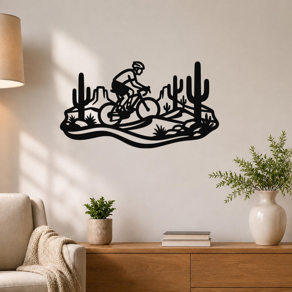 Black metal wall art silhouette of a cyclist on a mountain bike through a Sonoran desert landscape with saguaro cacti, mounted on a living room wall above a wooden console table.