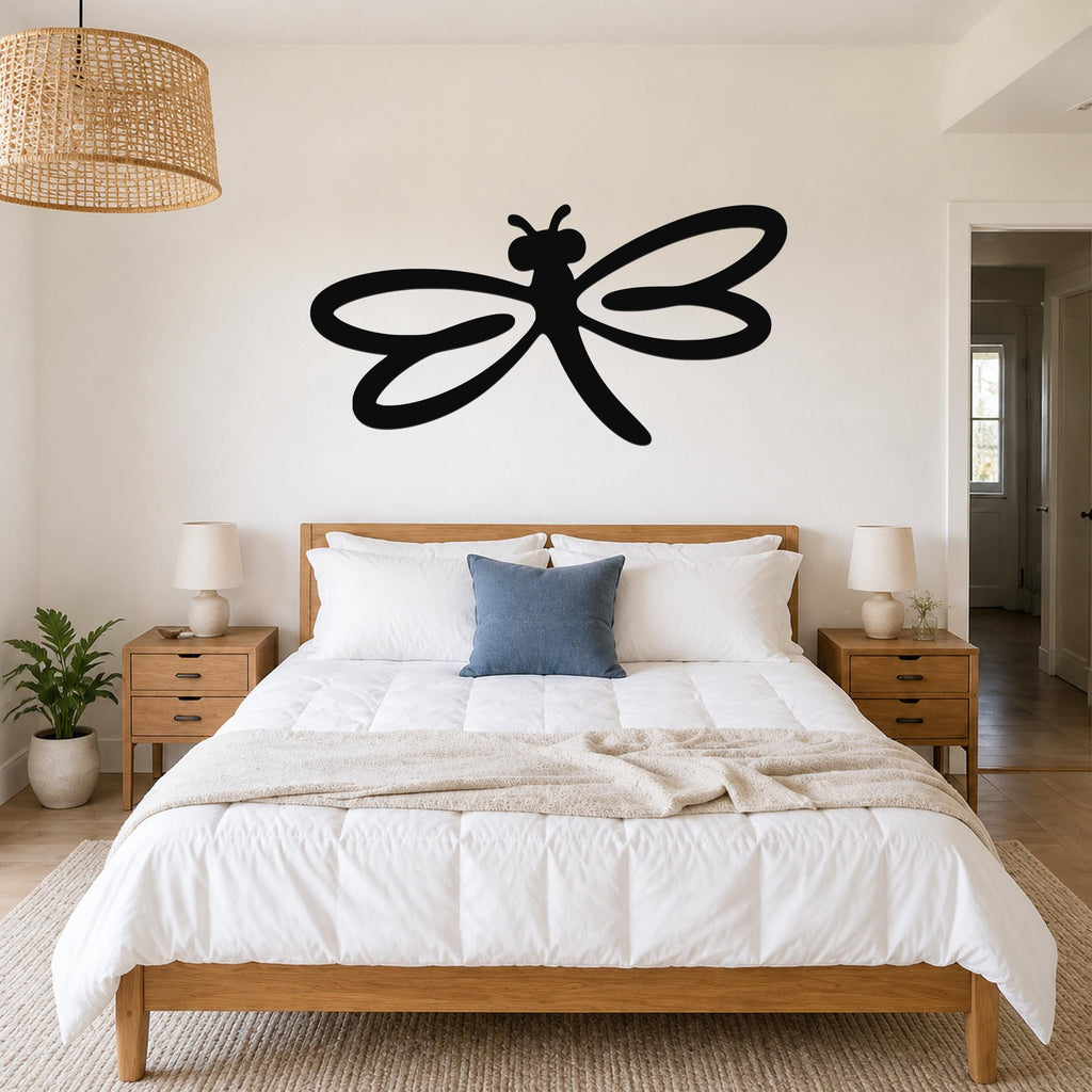 Black metal dragonfly wall art with flowing wing cutouts, mounted above a wooden bed in a bright bedroom.