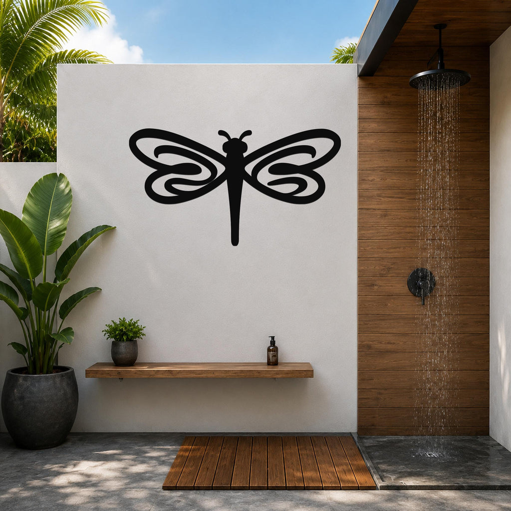 Black metal dragonfly wall art with intricate wing cutouts, mounted on a white outdoor wall above a wooden shelf in a patio shower area.