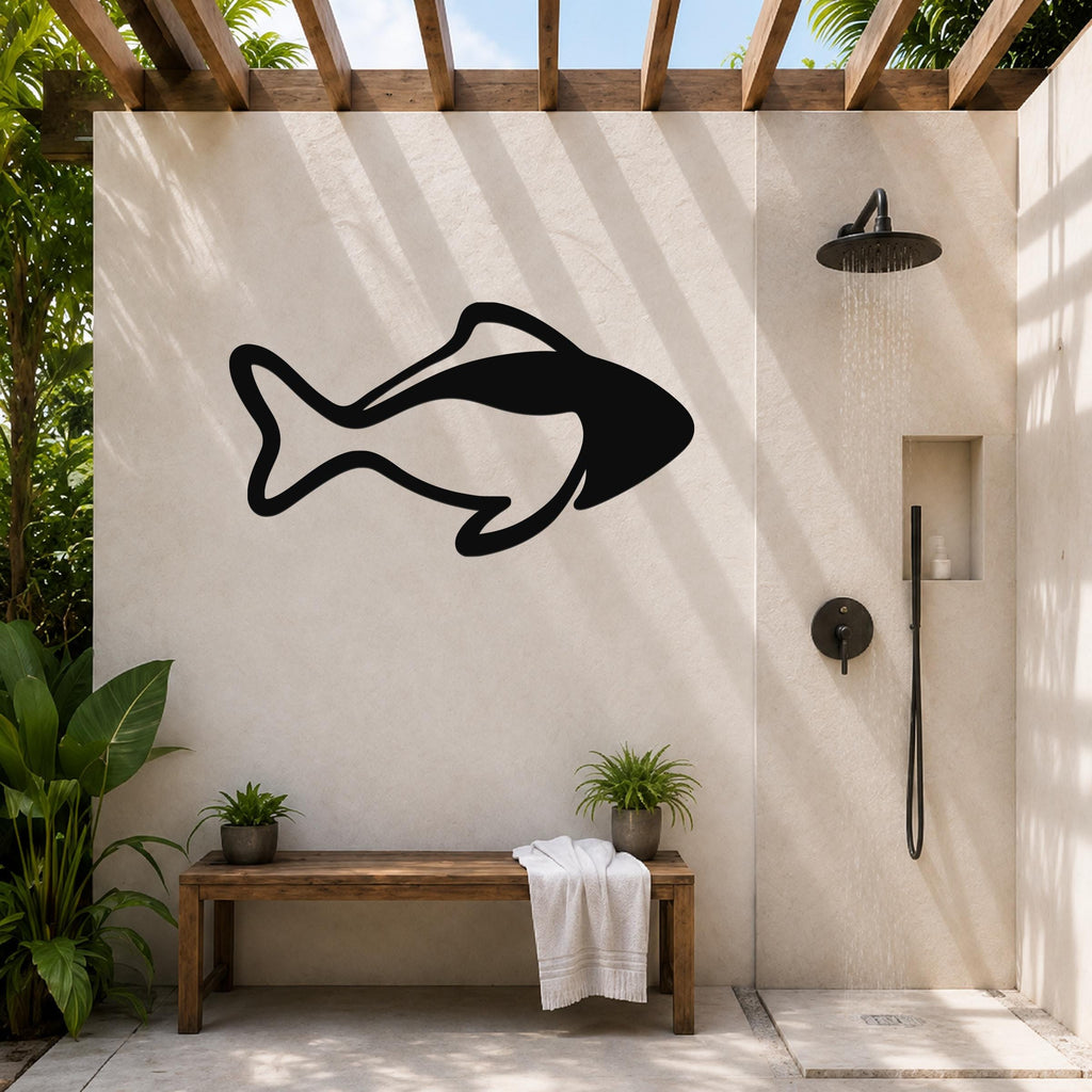 Black metal fish silhouette wall art mounted on a beige outdoor shower wall, with a wooden bench and potted plants below.