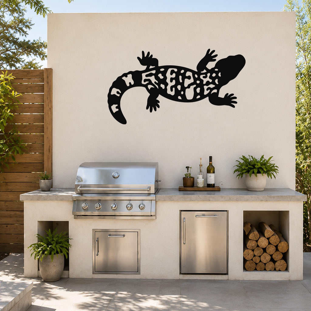 Black metal Gila monster wall art with intricate cutout patterns, mounted on an outdoor kitchen wall above a stainless steel grill and counter.