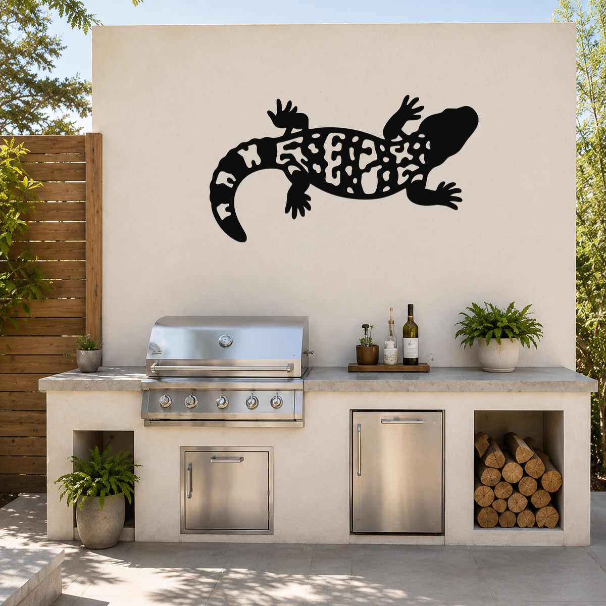 Black metal Gila monster wall art with intricate cutout patterns, mounted on an outdoor kitchen wall above a stainless steel grill and counter.