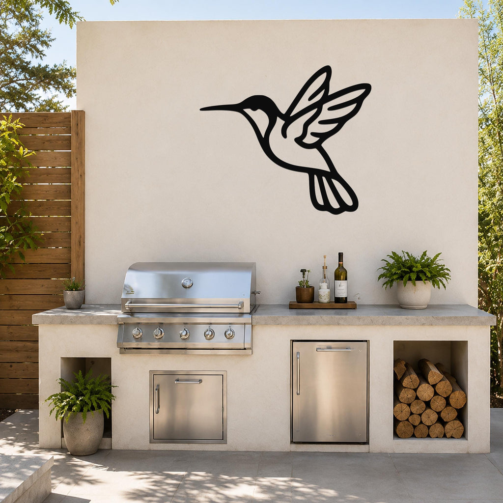 Black metal hummingbird wall art in silhouette form, mounted on an outdoor kitchen wall above a stainless steel grill and counter.