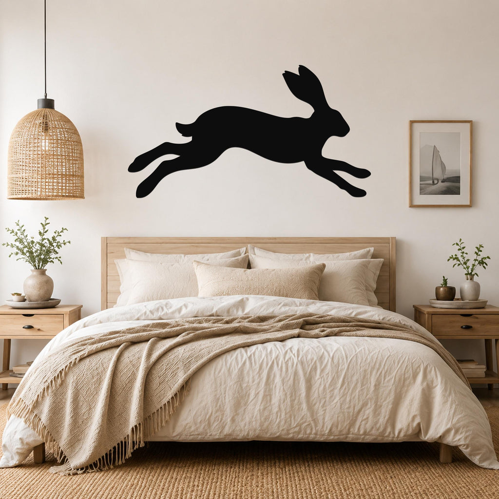Black metal jackrabbit wall art silhouette mounted above a bed in a neutral bedroom.
