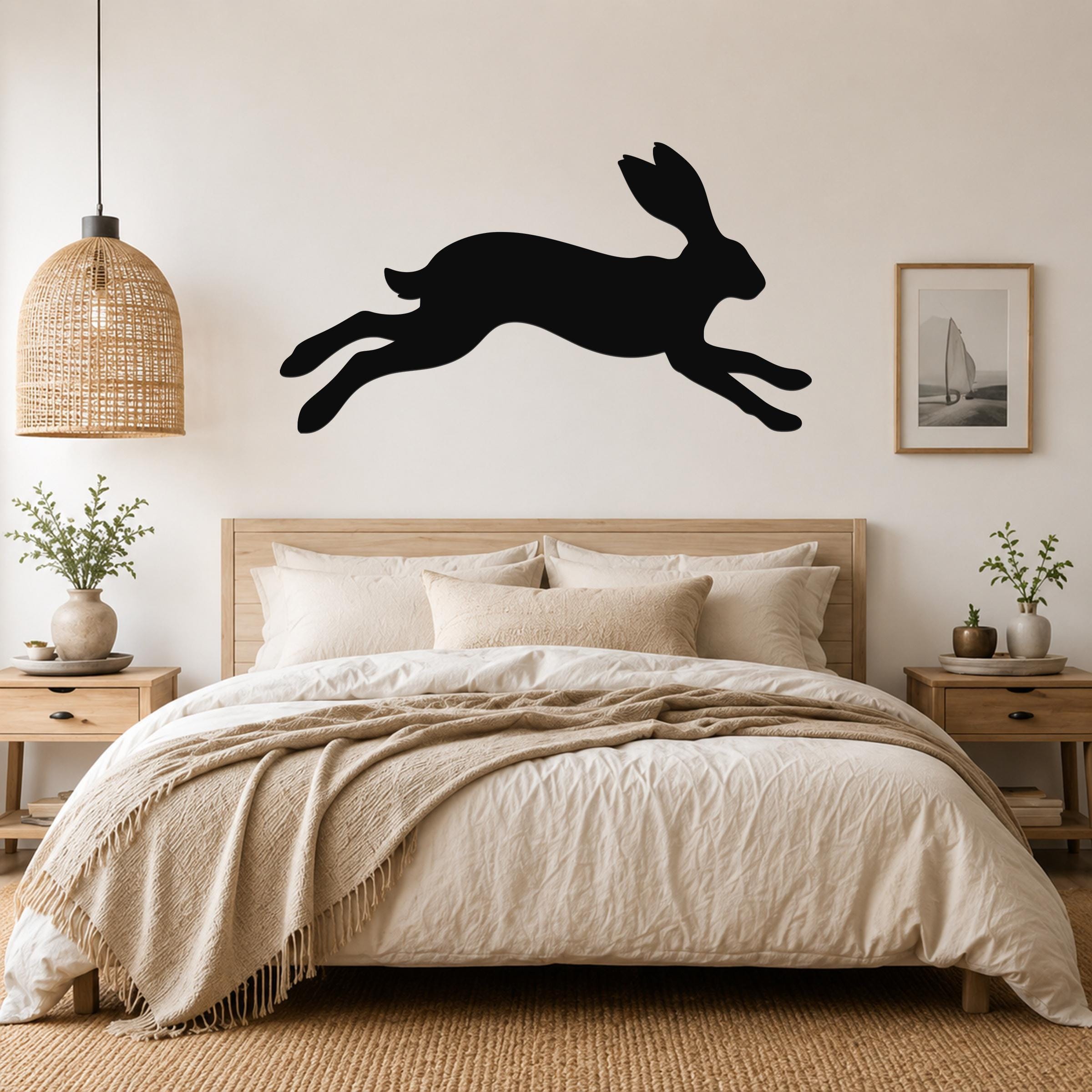 Black metal jackrabbit wall art silhouette mounted above a bed in a neutral bedroom.