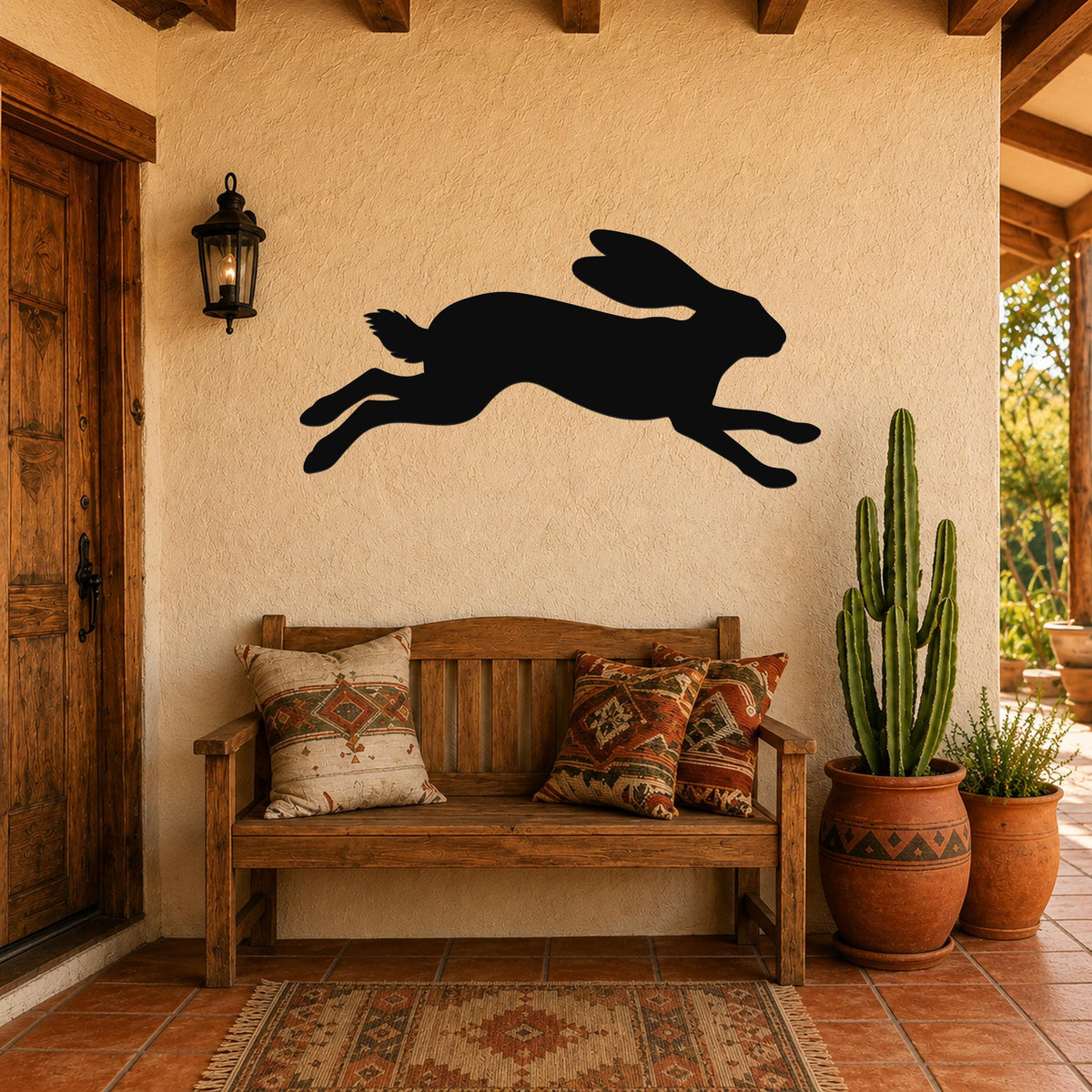 Black metal jackrabbit wall art silhouette with motion lines, mounted on a stucco wall above a wooden bench in a patio entryway.