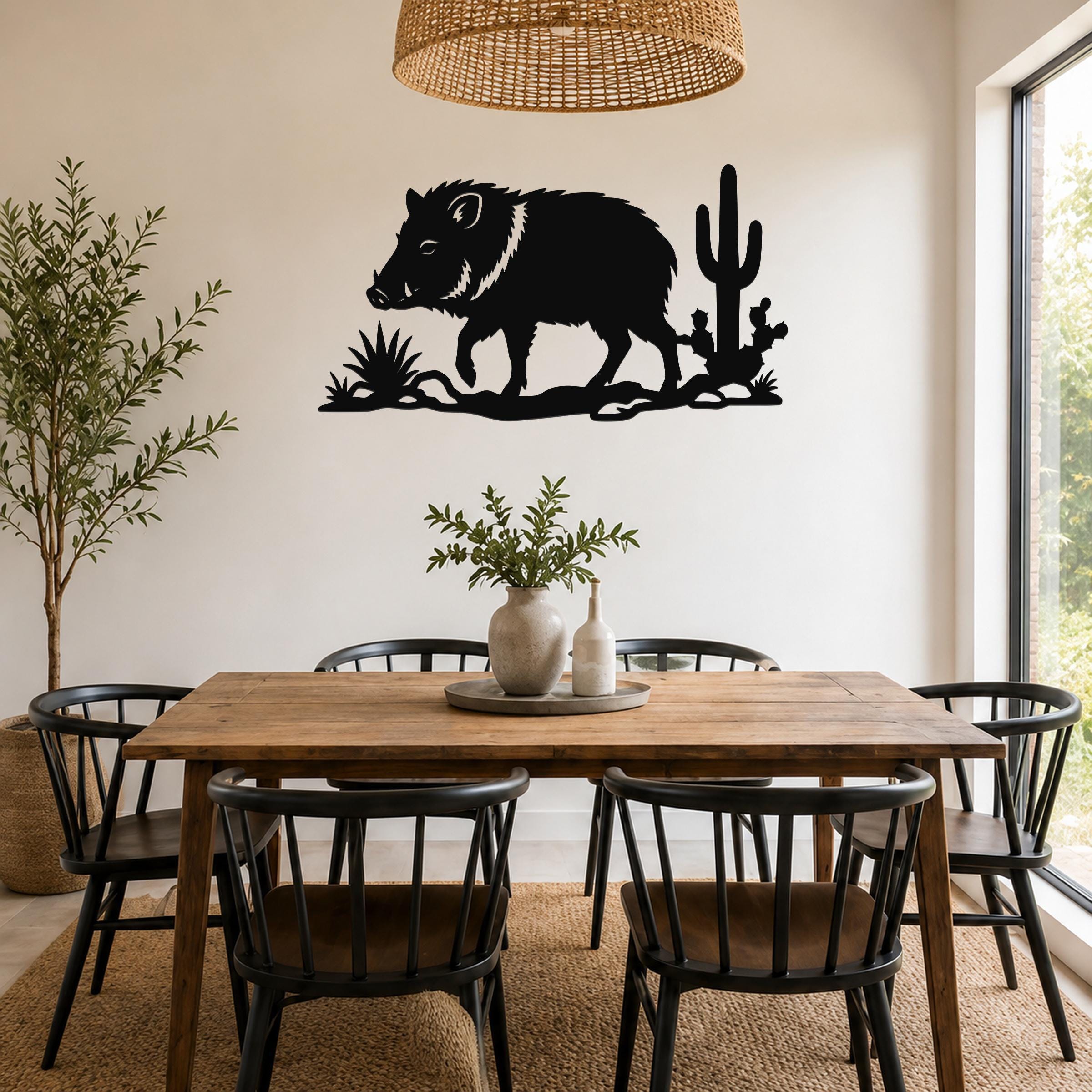 Black metal wall art silhouette of a javelina with cacti, mounted on a dining room wall above a wooden table.