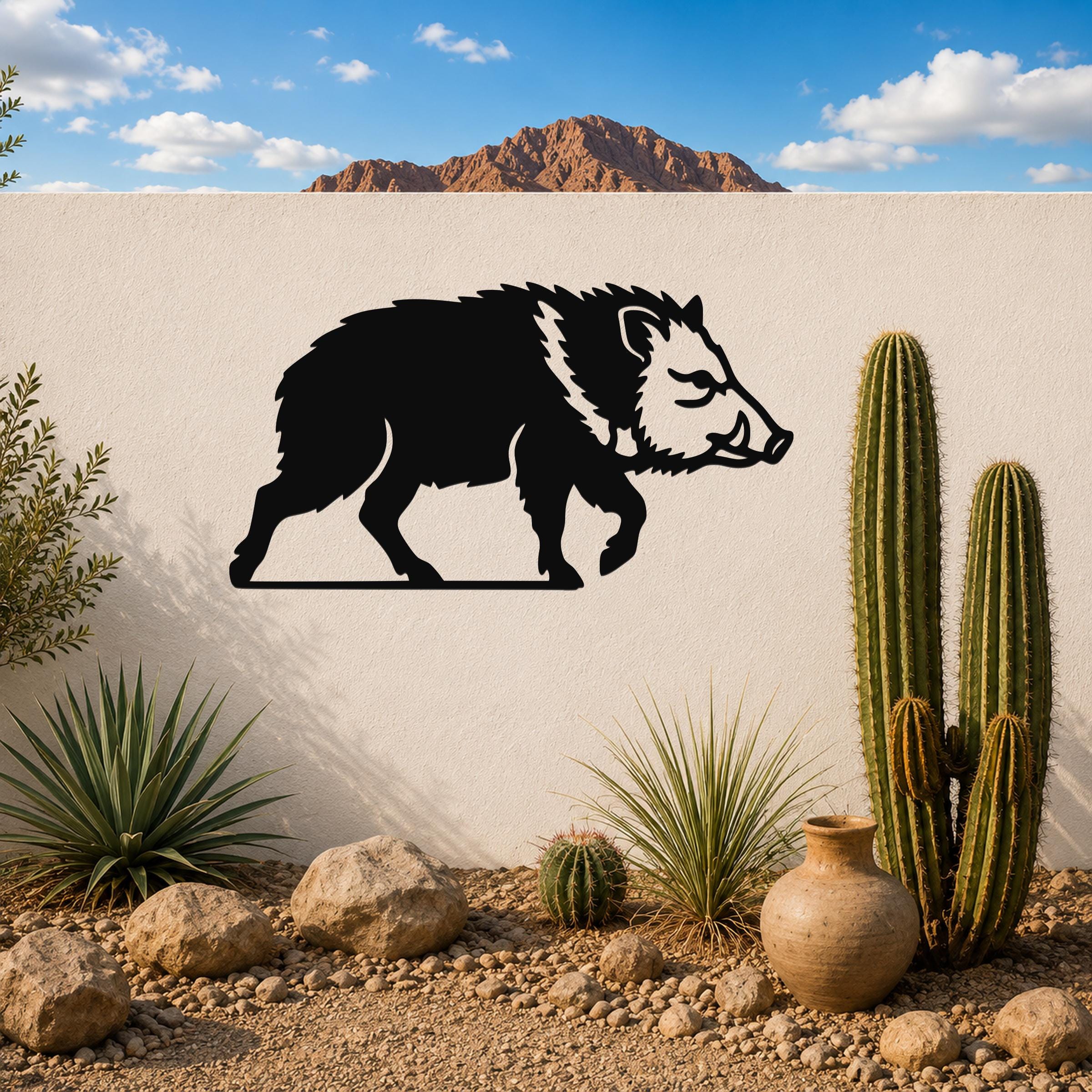 Black metal javelina wall art silhouette mounted on a white outdoor wall, displayed in a desert garden with cacti and rocks.