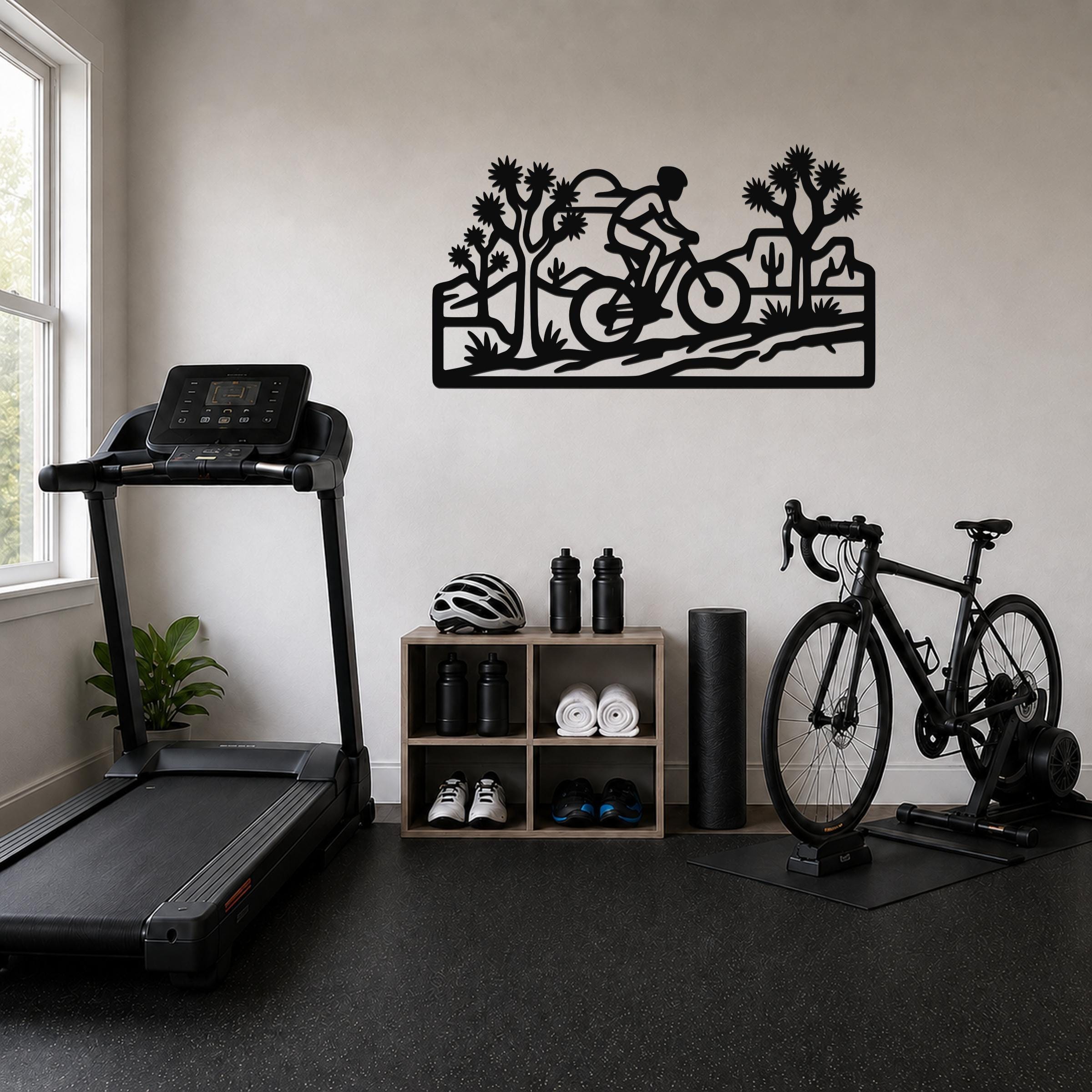 Black metal wall art with a cyclist silhouette and Joshua trees, mounted on a wall above a shelving unit in a home gym.