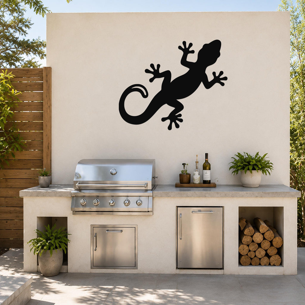 Black metal gecko wall art silhouette mounted on an outdoor kitchen wall above a stainless steel grill and countertop.