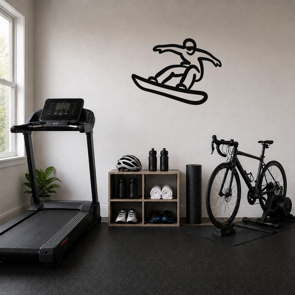 Black metal wall art silhouette of a snowboarder in motion, mounted on a light-colored wall above a wooden storage shelf in a home gym.