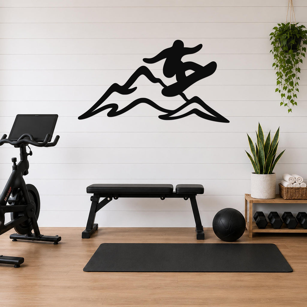 Black metal wall art silhouette of a snowboarder in motion over mountain peaks, mounted on a white shiplap wall above a workout bench in a home gym.
