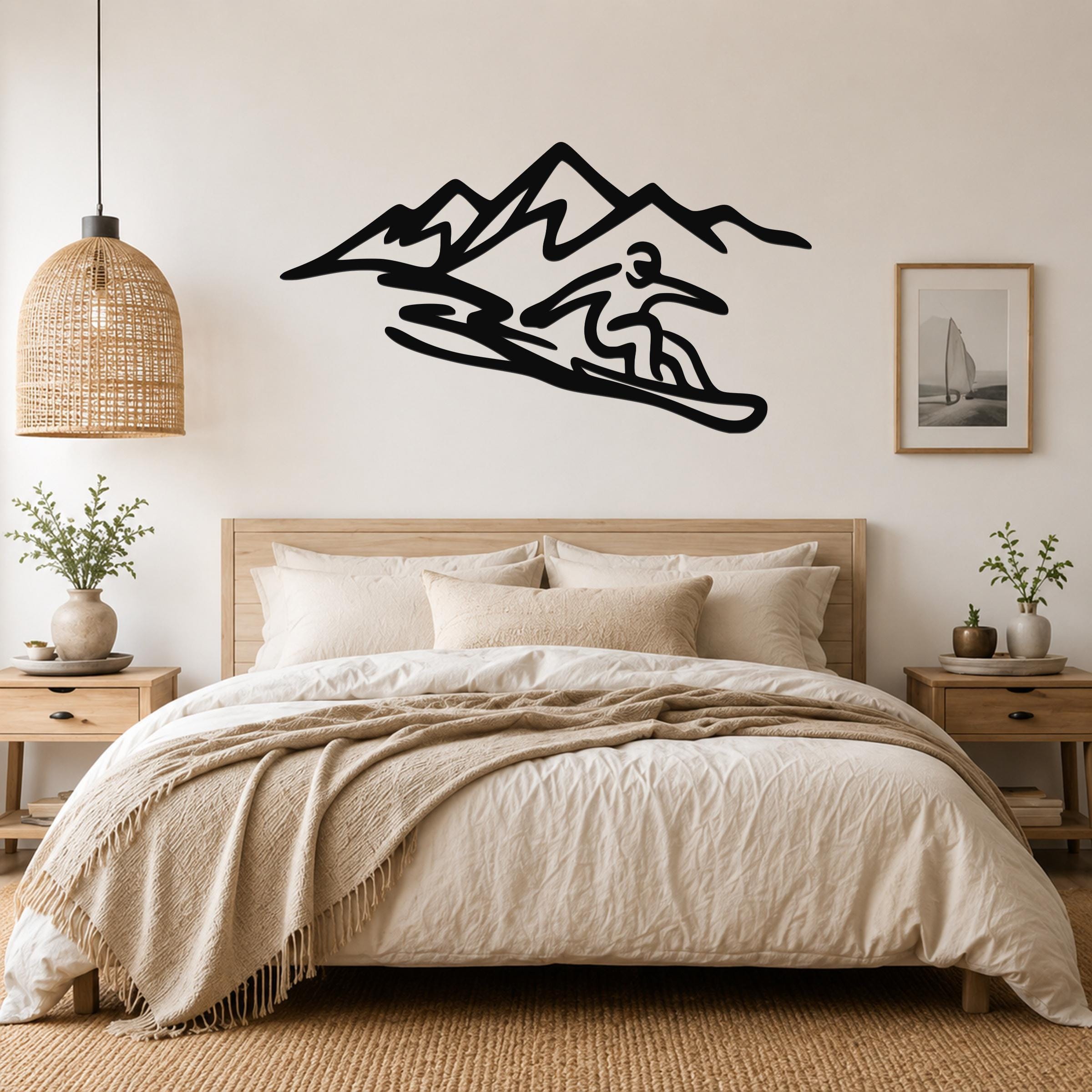 Black metal wall art silhouette of a snowboarder in motion with mountain peaks, mounted above a bed in a neutral bedroom.