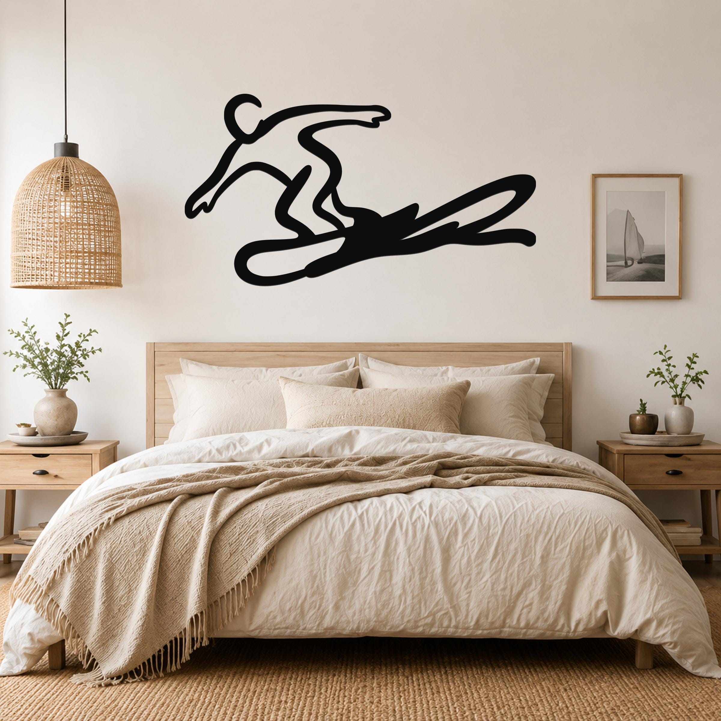 Black metal wall art silhouette of a snowboarder in motion, mounted above a bed in a neutral bedroom.