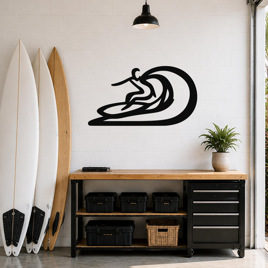 Black metal surfer wall sculpture with wave cutout, mounted on a white brick wall above a wooden workbench in a garage.