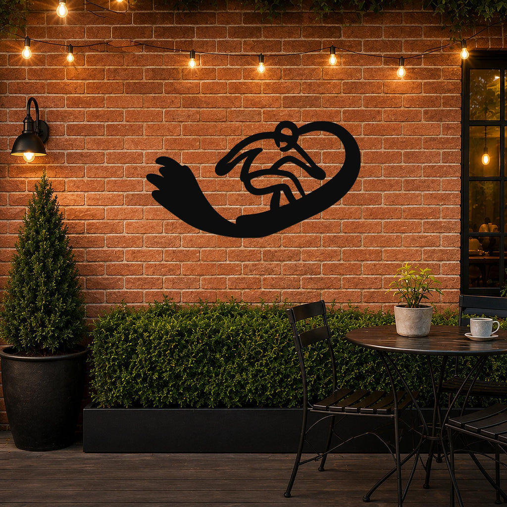 Black metal wall art silhouette of a snowboarder in motion, mounted on a brick patio wall above a small table and chairs.