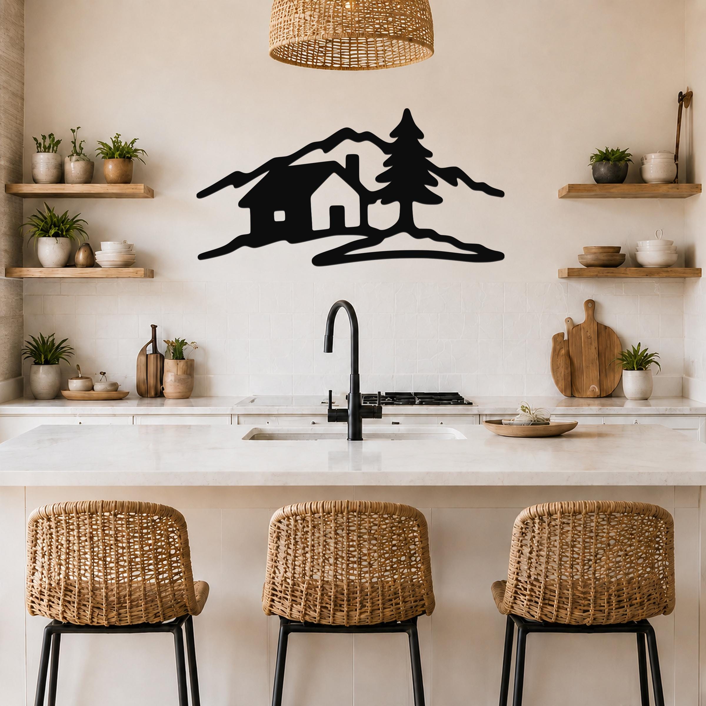 Black metal wall art cutout of a cabin, tree, and mountains, mounted above a kitchen counter with wicker bar stools and open shelves.