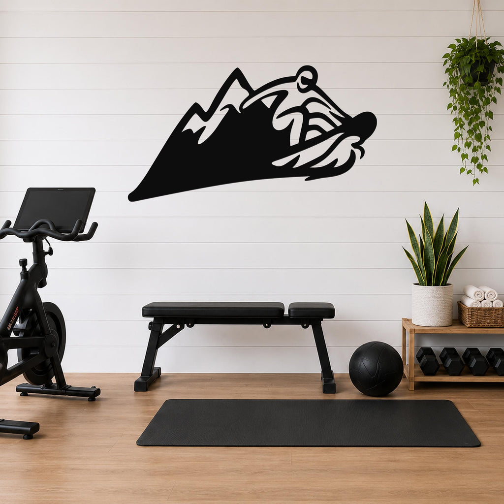 Black metal wall art featuring a snowboarder silhouette cutting through a mountain peak, mounted on a white shiplap wall above a workout bench in a home gym.