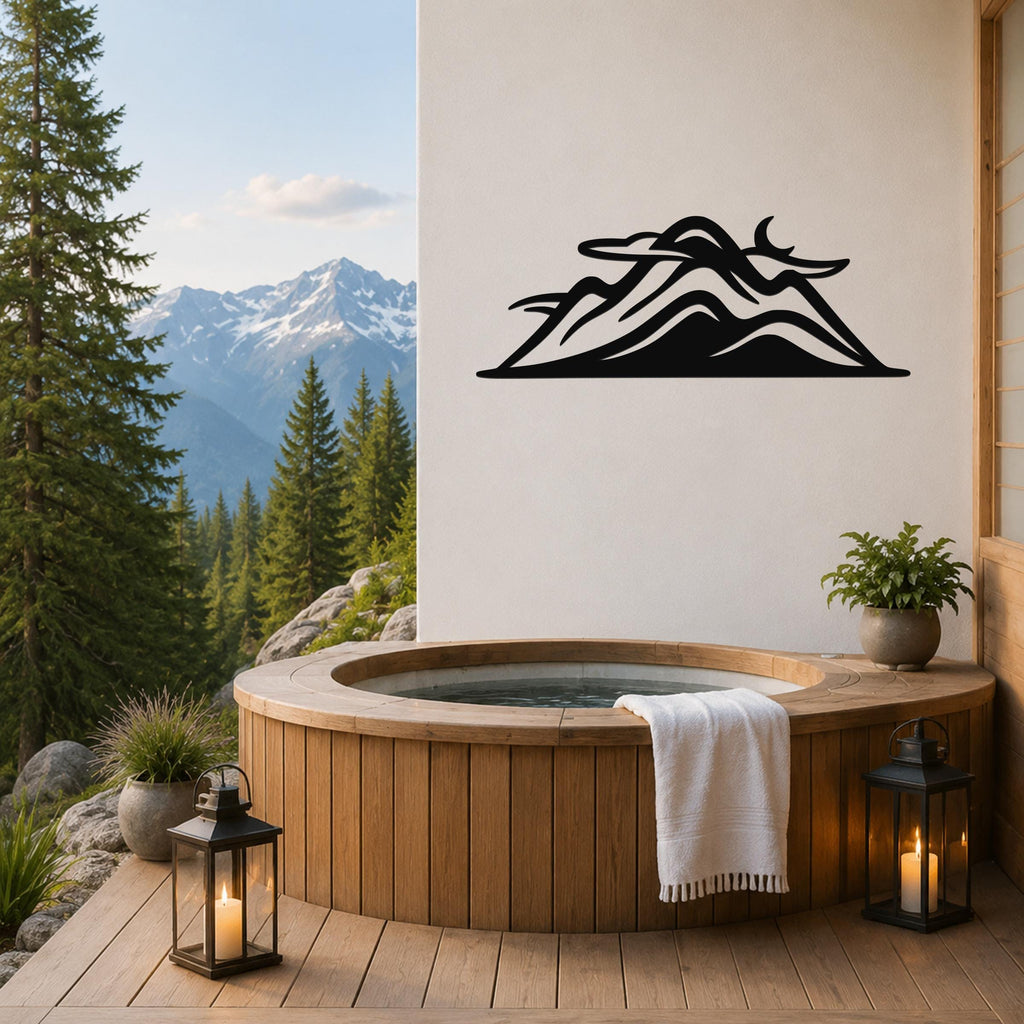Black metal mountain silhouette wall art with layered peaks and internal cutouts, mounted on a white wall above a wooden hot tub on a deck with a mountain view.