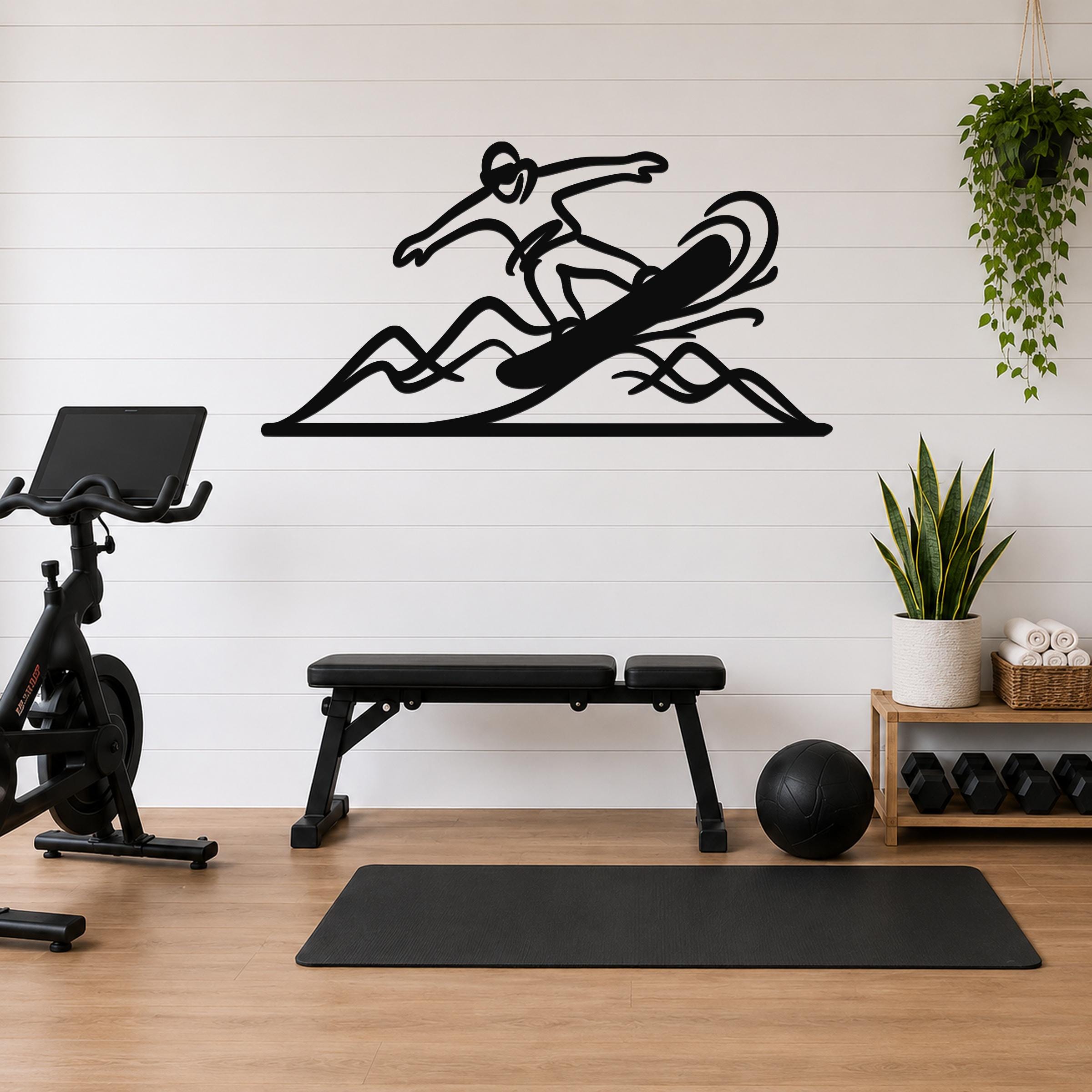 Black metal wall art cutout of a snowboarder in motion over mountain waves, mounted on a white shiplap wall above a workout bench in a home gym.