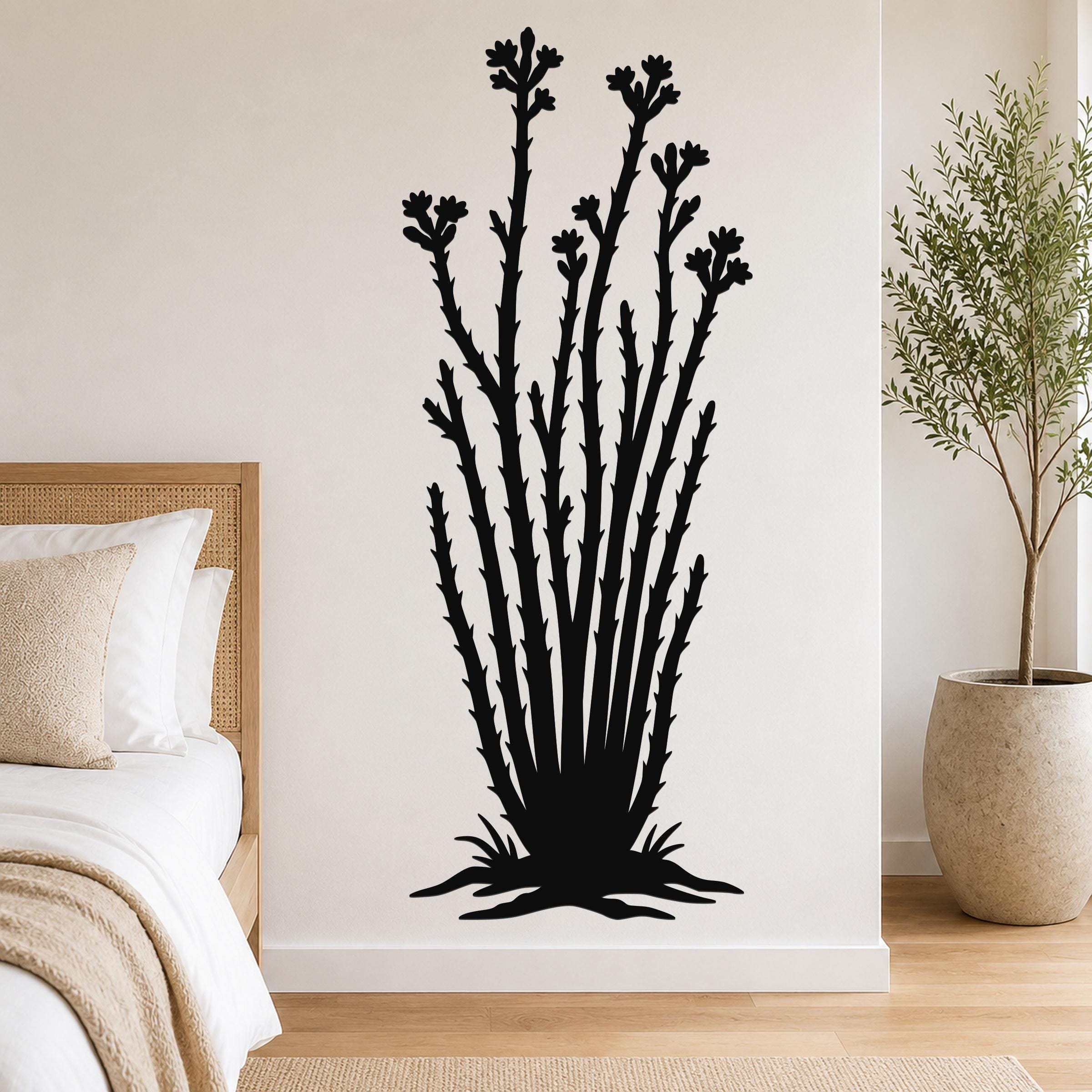 Black metal ocotillo wall art with flower and branch cutouts, mounted on a bedroom wall above a bed.