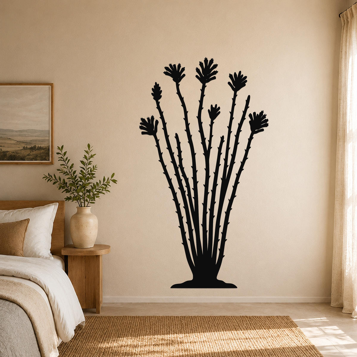 Black metal ocotillo wall sculpture with spiny stems and flower cutouts, mounted on a beige bedroom wall above a woven rug.