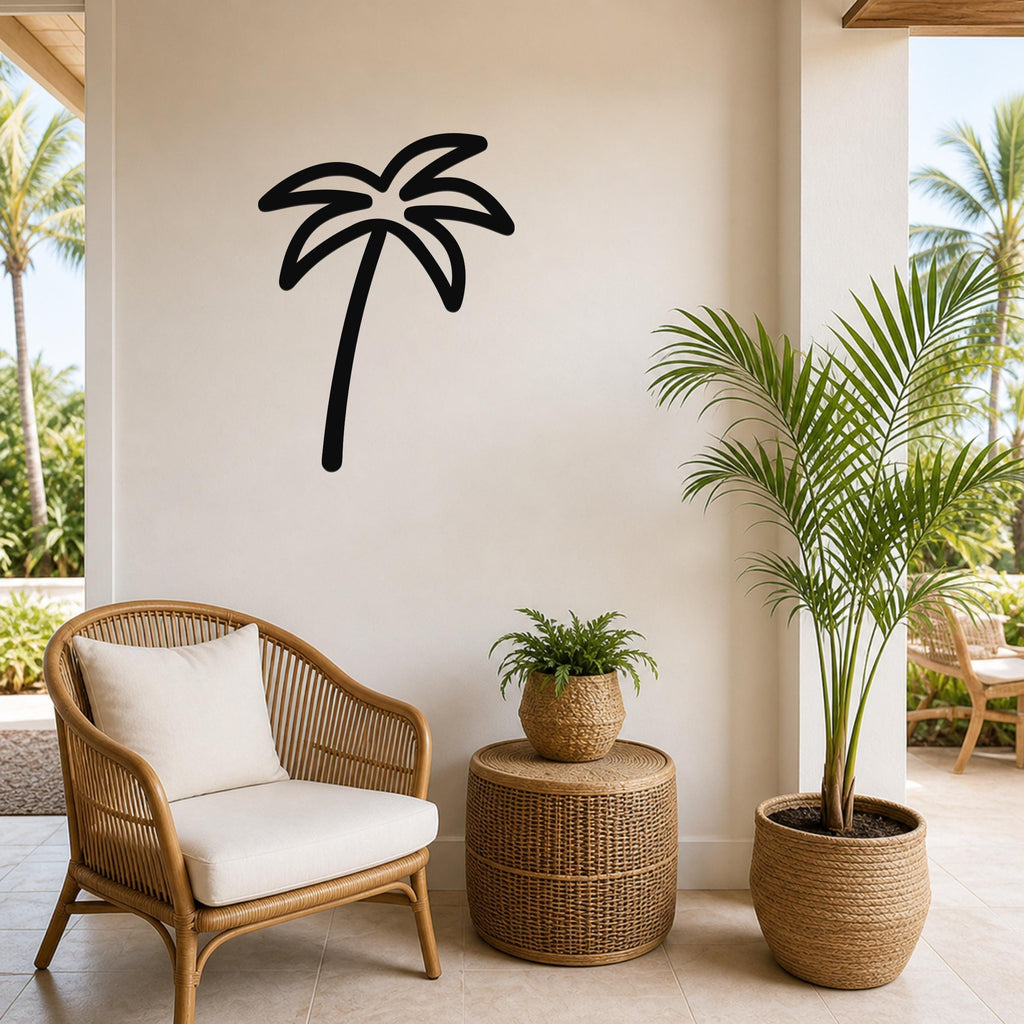 Black metal palm tree wall art silhouette mounted on a light-colored wall above a wicker chair and potted plants in a tropical patio setting.
