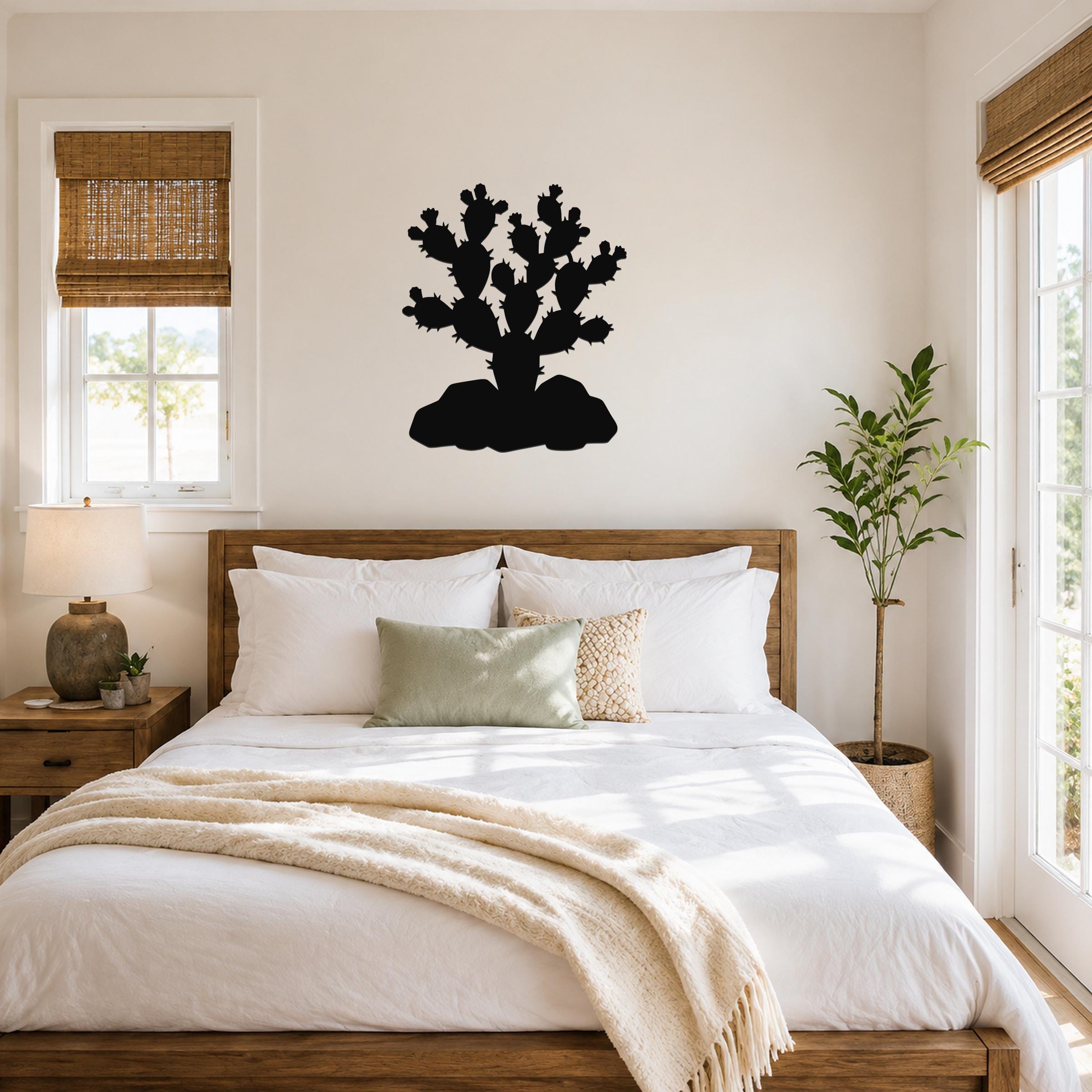 Black metal prickly pear cactus wall art silhouette mounted above a wooden bed in a bright bedroom.