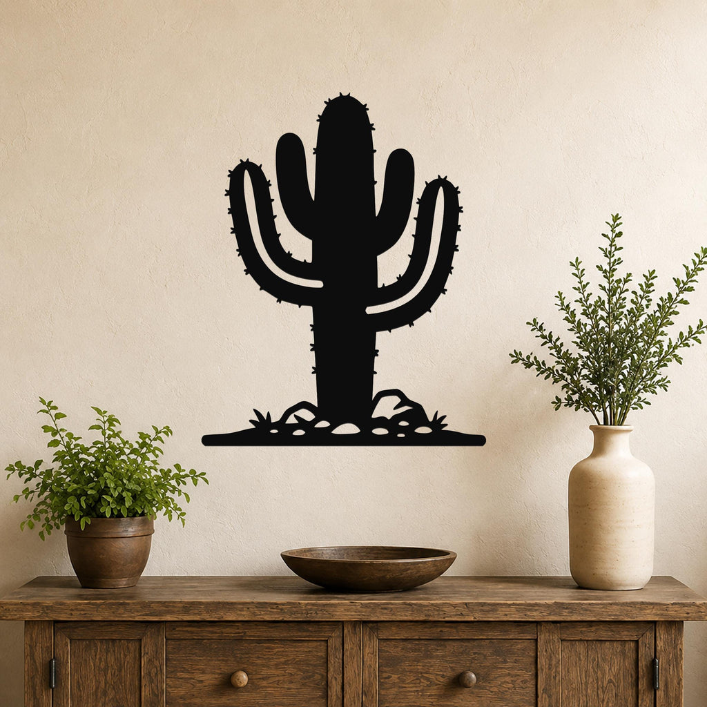 Black metal wall art cutout of a saguaro cactus with spines and rocks, mounted on a beige wall above a wooden console table with plants.