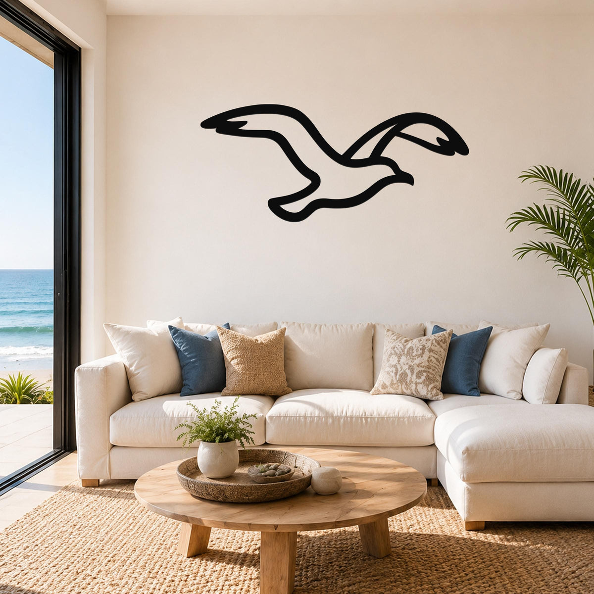 Black metal seagull wall art with motion-line cutouts, mounted above a white sofa in a living room with ocean views.