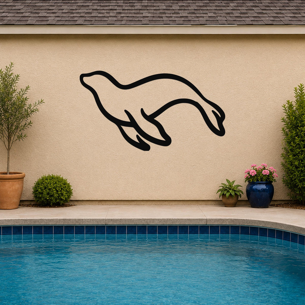 Black metal sea lion wall art silhouette mounted on a beige outdoor wall above a pool, with potted plants nearby.