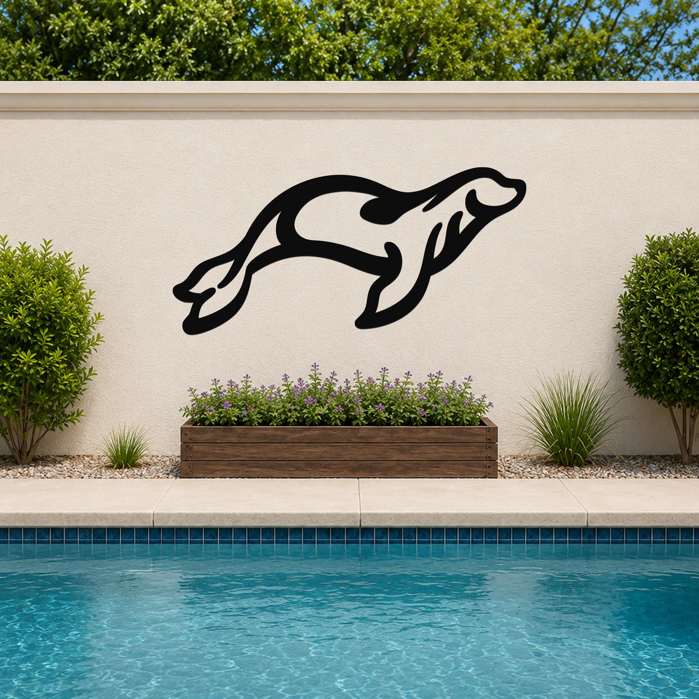 Black metal sea lion wall art in a leaping silhouette, mounted on an outdoor wall above a planter and pool.