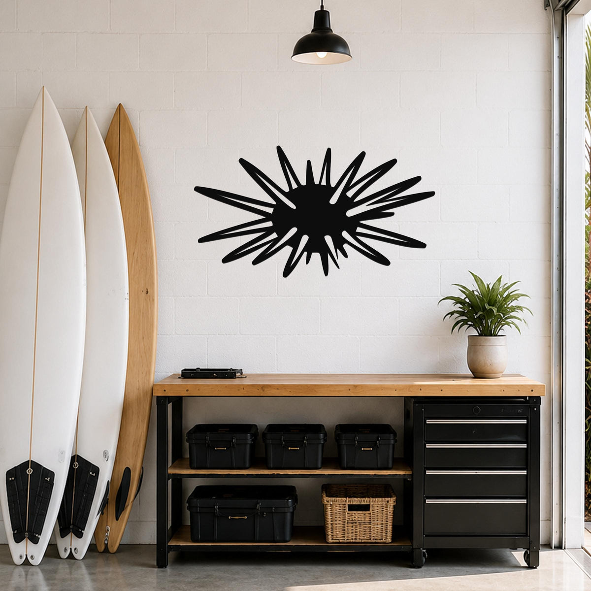Black metal sea urchin wall art with spiky radial cutouts, mounted on a white brick wall above a wooden workbench in a garage.