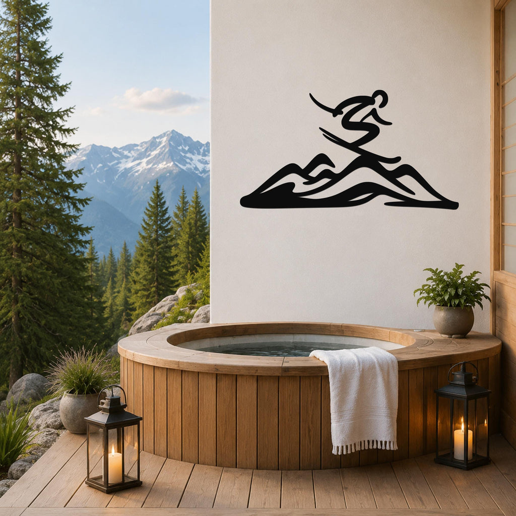 Black metal wall art of a skier silhouette above mountain peaks, mounted on a white wall above a wooden hot tub on a deck with a mountain view.