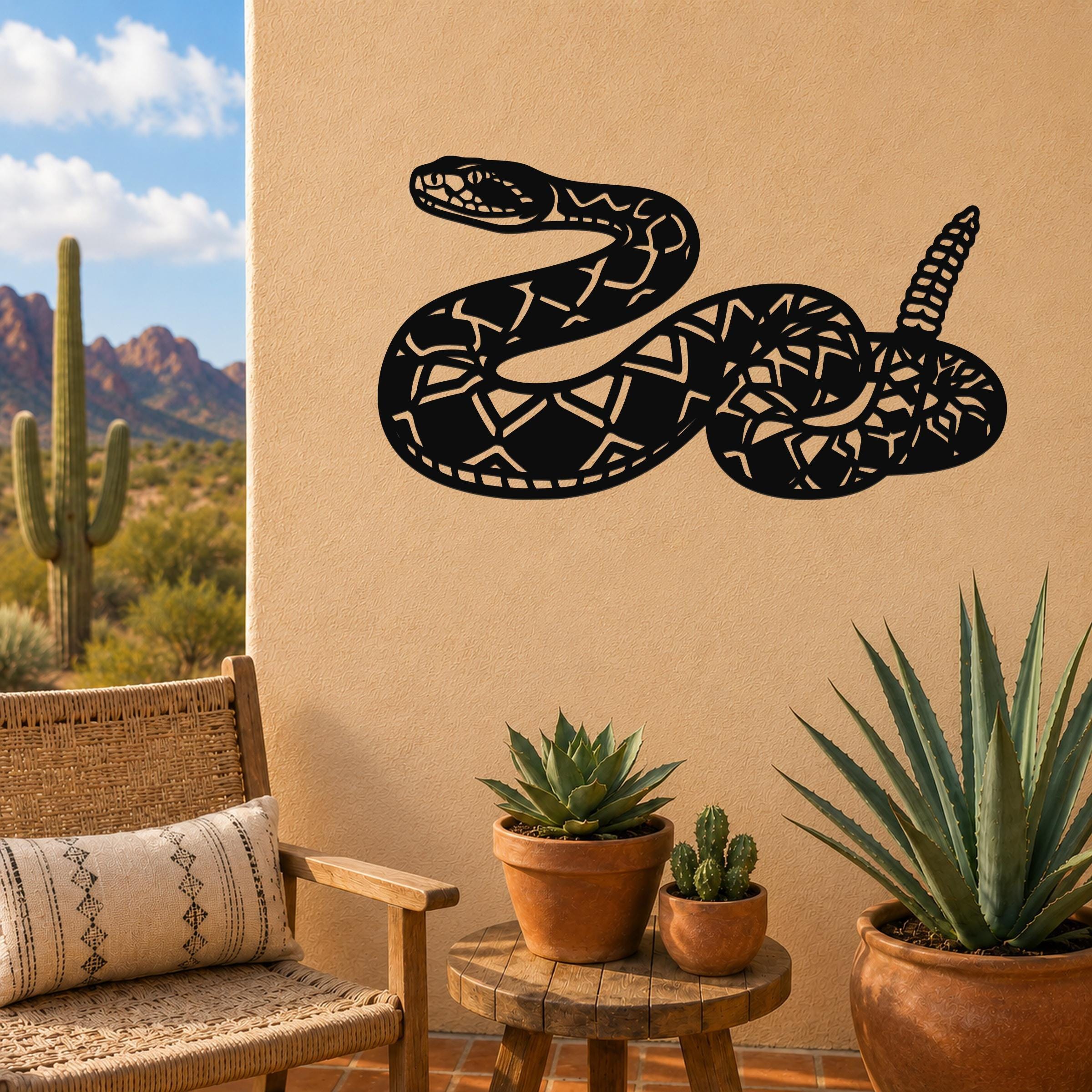 Black metal snake wall art with intricate geometric cutouts, mounted on a beige outdoor wall above a small wooden table with potted succulents.
