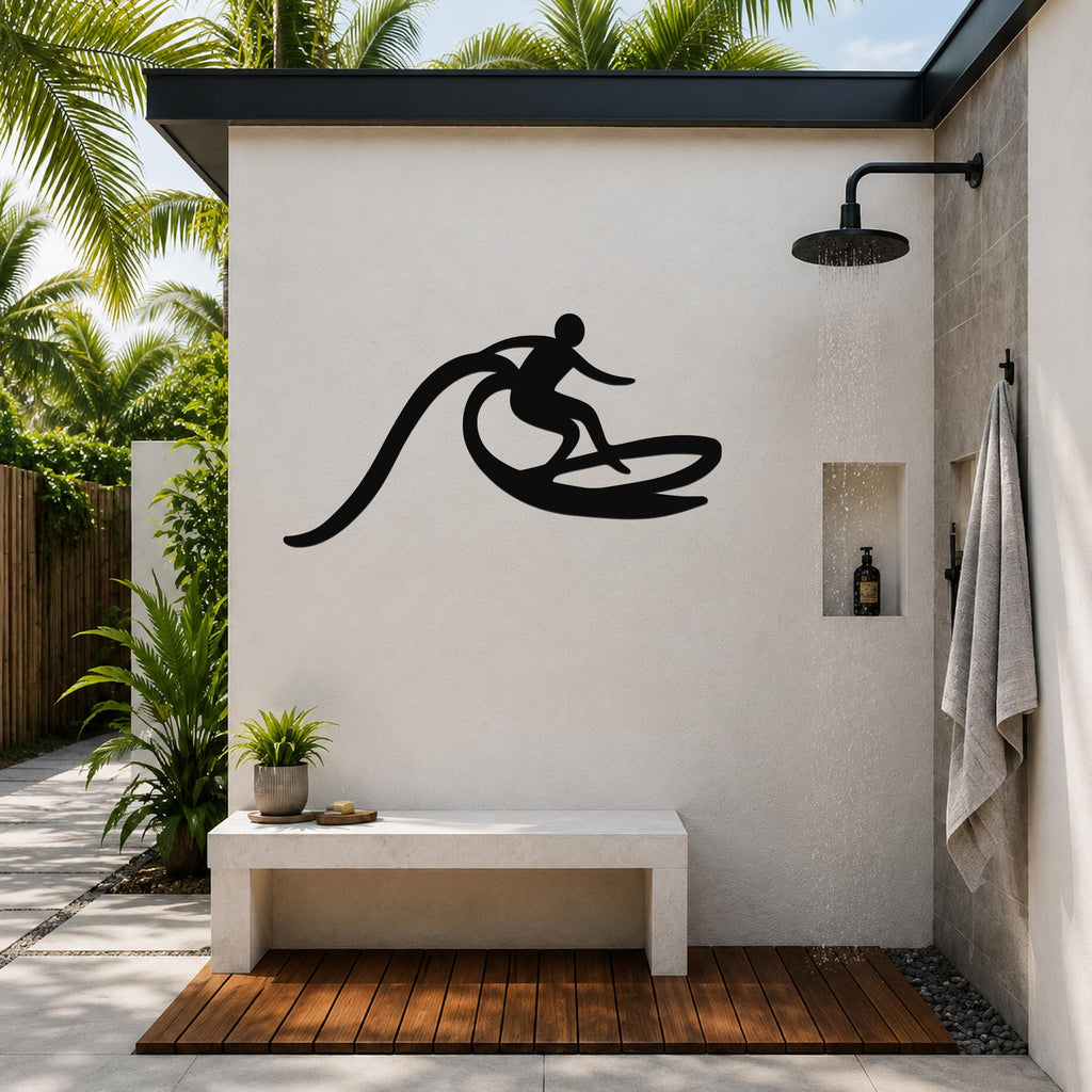Black metal surfer wall art with motion-line cutouts, mounted on an outdoor shower wall above a bench in a tropical patio setting.
