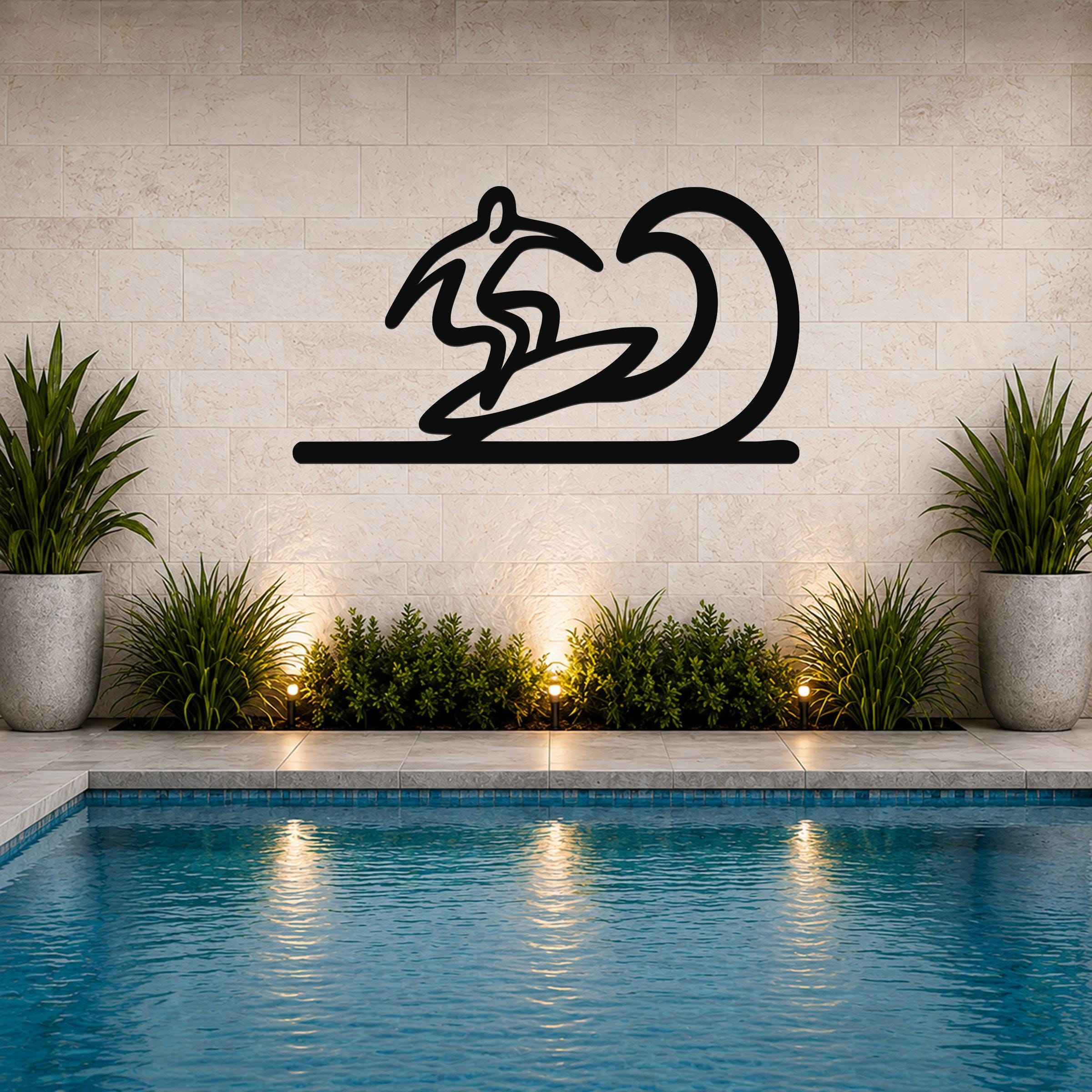 Black metal surfer wall art with a wave silhouette, mounted on a tiled wall above a pool with potted plants and ground lights.
