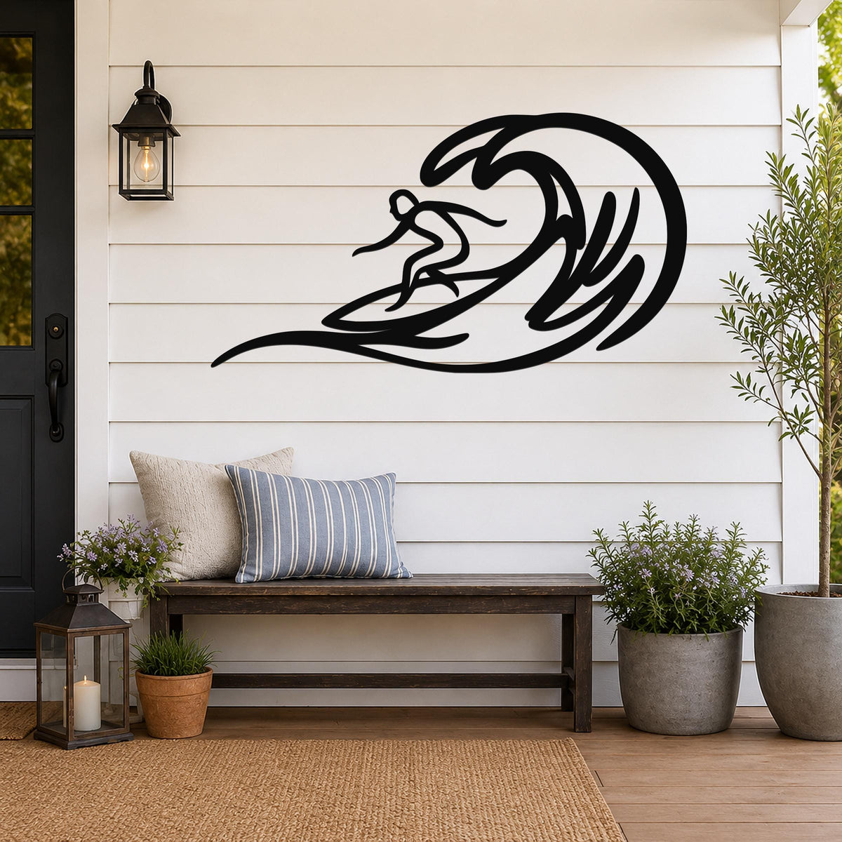 Black metal surfer wall art with wave cutout, mounted on a white shiplap wall above a wooden bench on a porch.